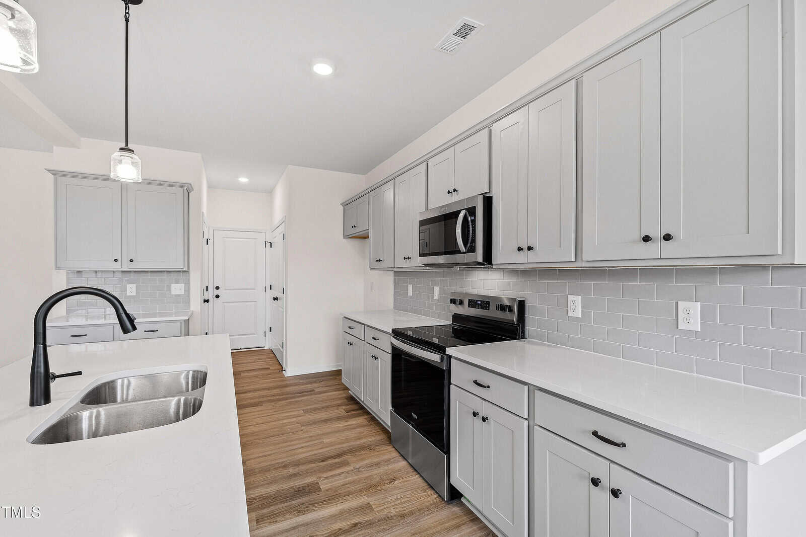 Modern kitchen with light gray cabinets, white countertops, stainless steel appliances, subway tile backsplash, black faucet on a double sink, and wood-look flooring. Bright, clean, and minimalistic design.