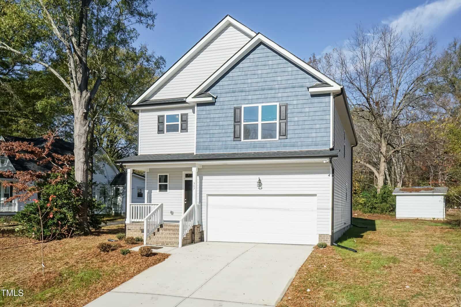 Two-story suburban house with gray-blue siding on the upper level, white siding on the lower level, a two-car garage, front porch, and a small detached shed in the backyard, surrounded by trees and grass.