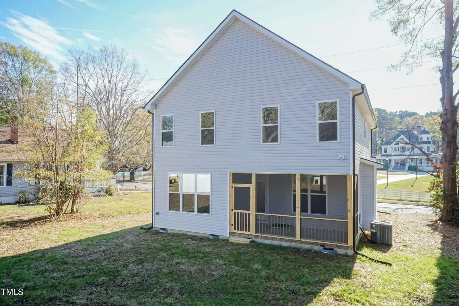 A two-story white house with large windows and a screened-in porch in the backyard, surrounded by grass and trees on a sunny day.