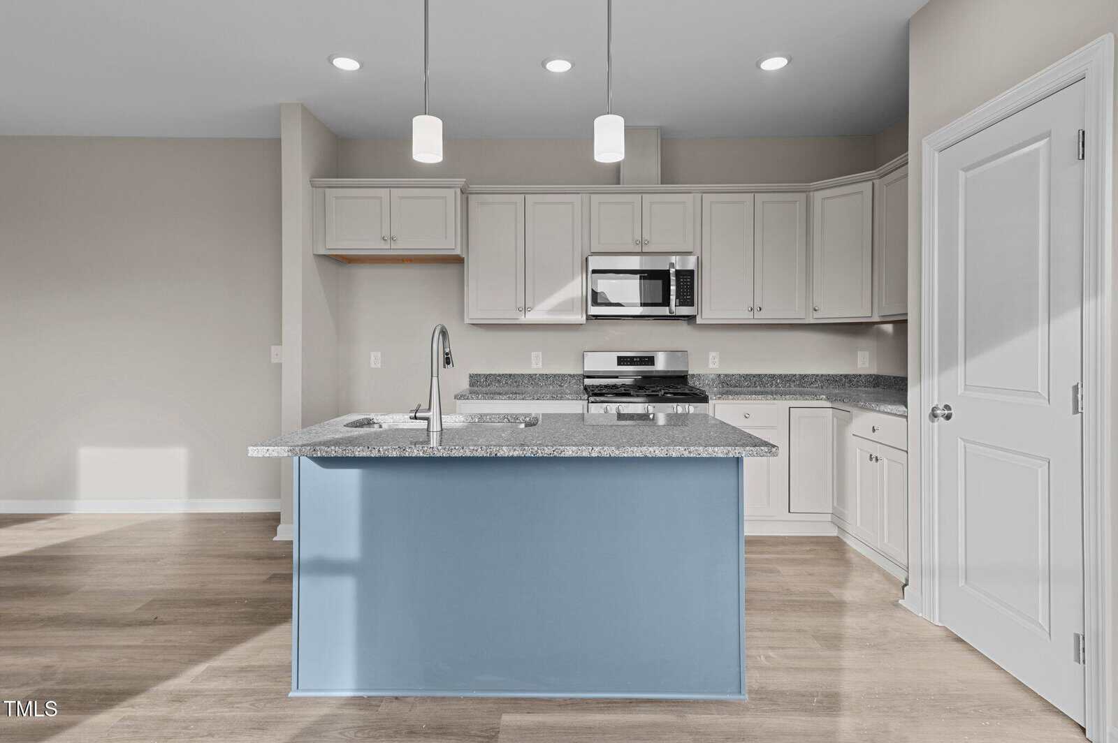 Modern kitchen with light gray cabinets, stainless steel appliances, granite countertops, a center island with a blue base, two pendant lights, and light wood flooring. The room is well-lit with recessed ceiling lights.