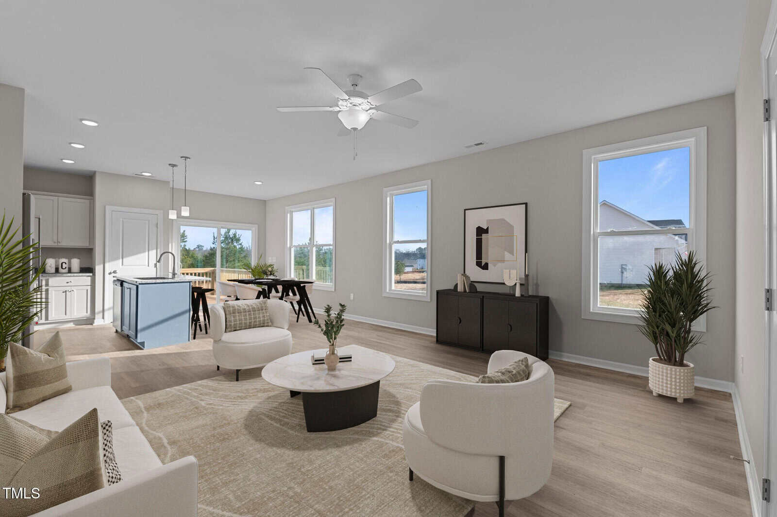 Modern open-concept living room and kitchen with neutral decor, light wood flooring, white walls, large windows, and minimalistic furniture. Dining area and kitchen are visible in the background.