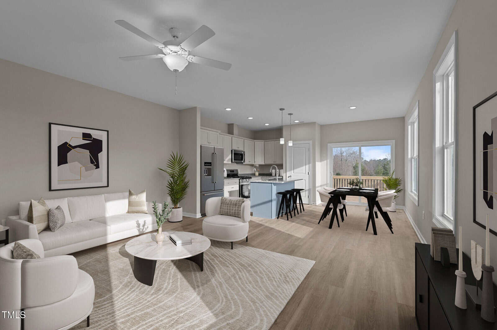 Open-concept living area with a white sofa, armchairs, and round coffee table; kitchen with light cabinetry and island; dining area with black table and chairs; large windows provide natural light and outdoor view.