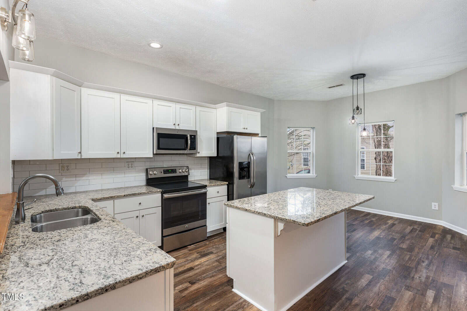 Modern kitchen with white cabinets, stainless steel appliances, granite countertops, a center island, subway tile backsplash, and dark wood flooring, with windows providing natural light.