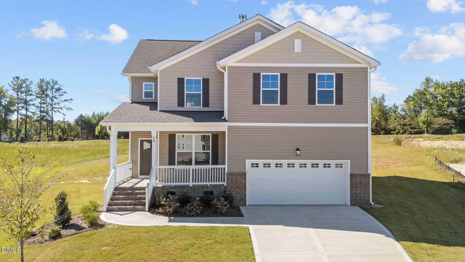 A modern two-story beige house with white trim, a front porch, and dark shutters. The home has a double garage, a sloped driveway, manicured landscaping, and sits on a grassy lot with trees in the background.
