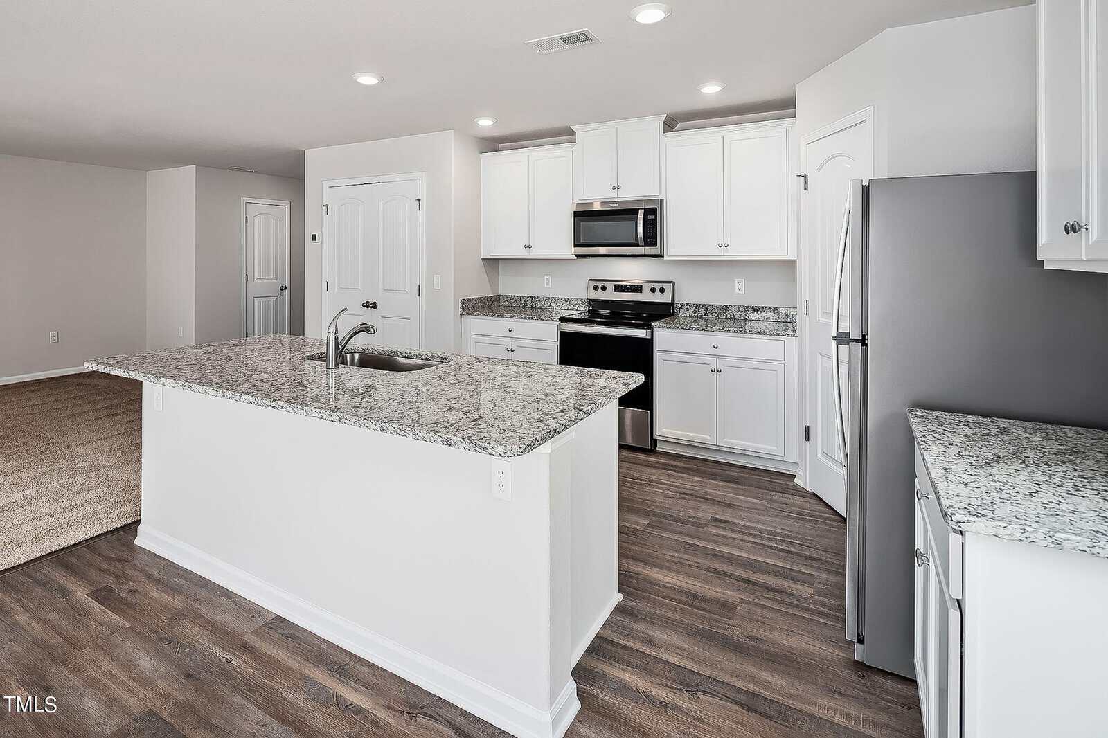 A modern kitchen with white cabinets, granite countertops, and stainless steel appliances. The space includes a large island with a sink, wood-style flooring, and recessed lighting.