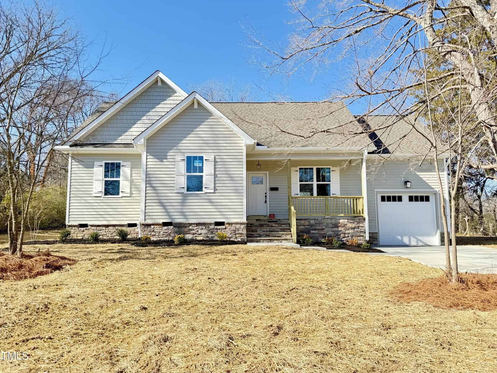Located at 107 Railroad Avenue, this single-story white house in Oxford boasts a gable roof and stone-accented facade. It features a cozy front porch with railing, a single garage door on the right, and is surrounded by bare trees on a modest lawn.