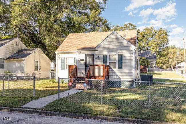 Nestled at 427 N Clark Street, this charming single-story house in Henderson boasts beige siding, a gable roof, and a wooden porch. A chain-link fence encloses the property, with a concrete path guiding you to the front steps. Trees and neighboring homes add to its quaint appeal.