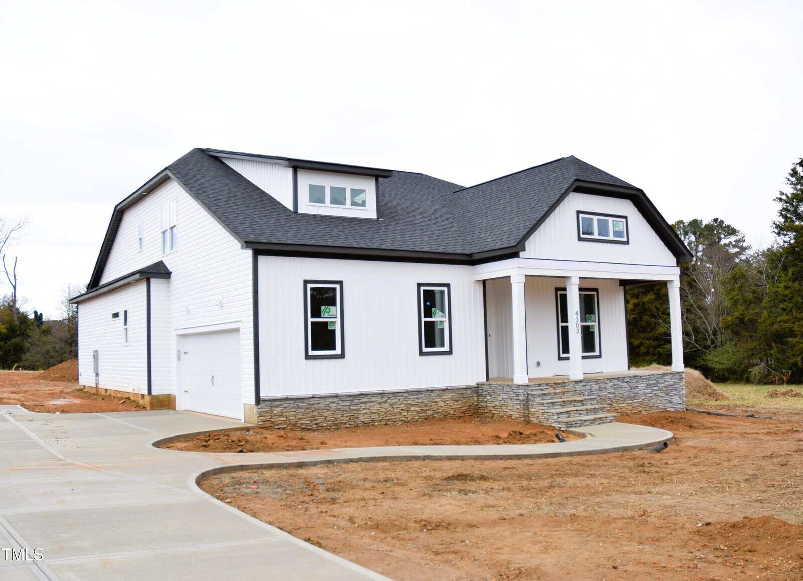 A two-story white house at 4303 Bragg Farm Lane in Franklinton is under construction, boasting a black roof and white trim. It features a front porch with columns, a two-car garage, and a newly paved driveway. The surrounding area remains bare earth, hinting at an unfinished yard.