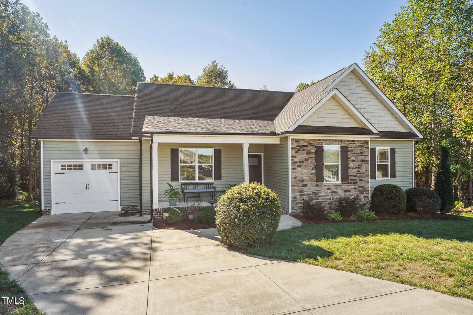 Nestled on 300 Wick Road, this charming single-story house boasts gray siding and stone accents under a gabled roof. With a one-car garage and inviting front porch, the home is framed by a well-maintained lawn and lush foliage, basking in the sunlight.