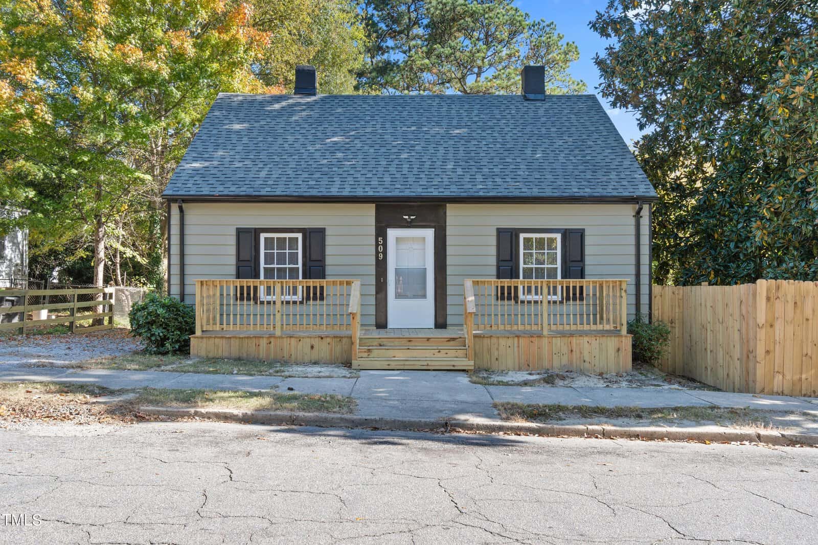 Located at 509 Zene Street in Henderson, this small, charming house boasts a light gray exterior with a dark roof. It features a wooden front porch and black shutters on the windows. The yard is enclosed by a wooden fence, with trees beautifully surrounding the property.