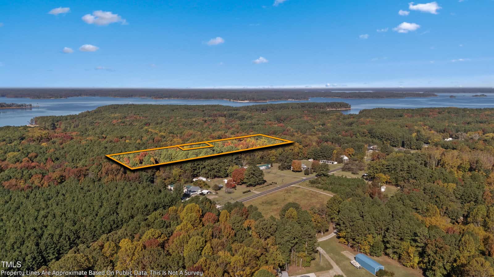 Aerial view of a forested area near Manson, showcasing a rectangular section amidst autumn-colored trees. A few houses dot the landscape, with a large body of water in the background under a blue sky.
