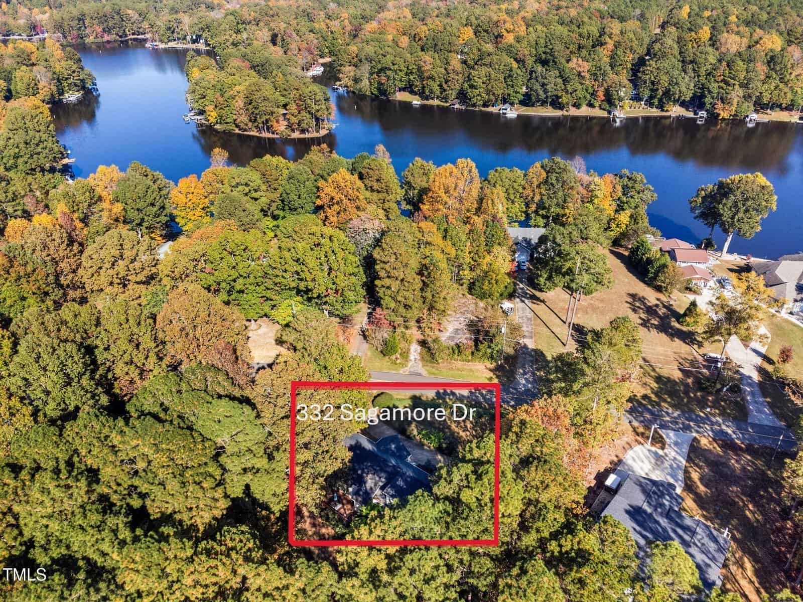 Aerial view of a tree-lined neighborhood by a lake, with a house at “332 Sagamore Dr” highlighted in a red box. Nearby homes, roads, and lakefront are visible amid autumn foliage.