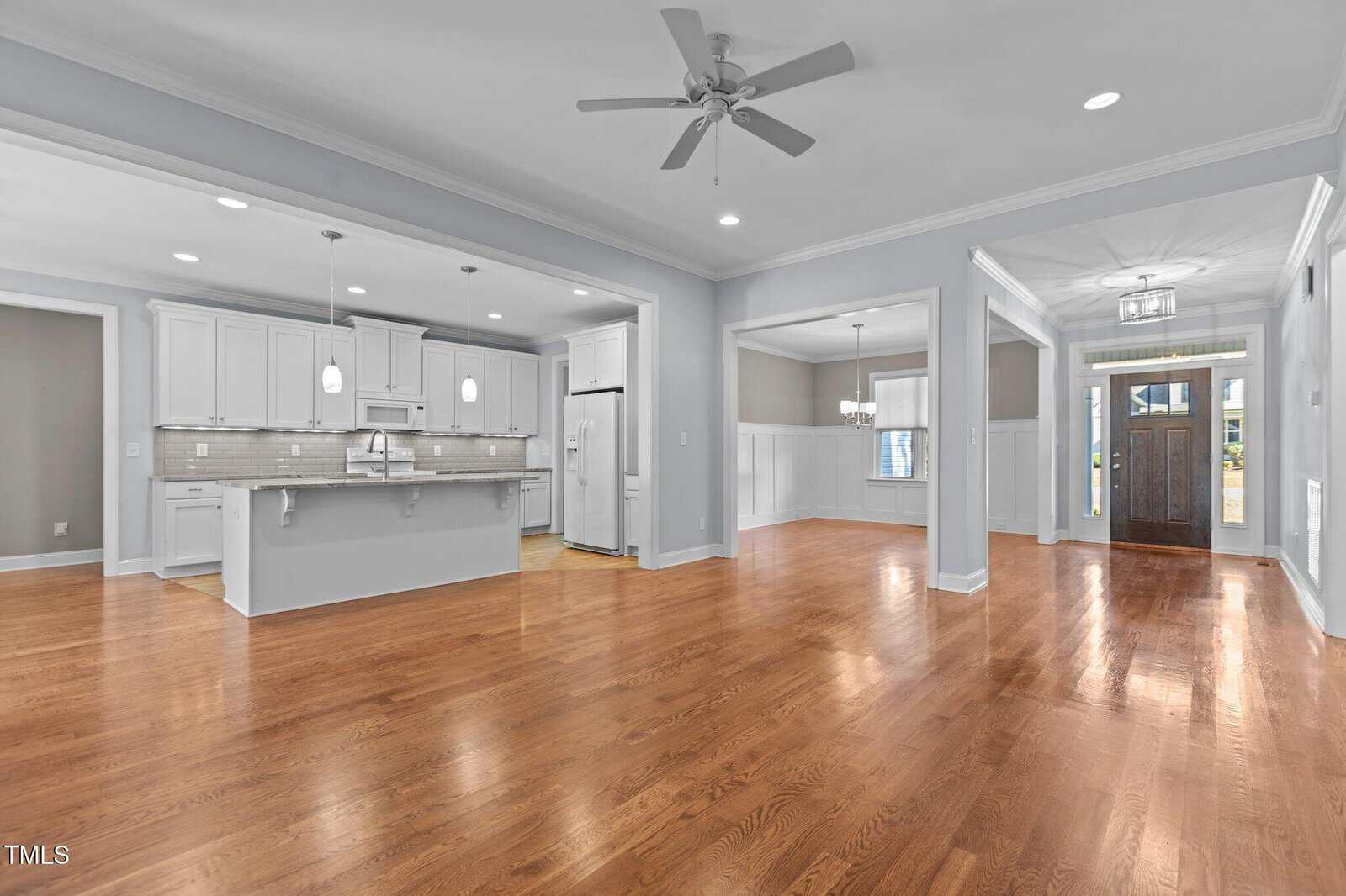 Spacious open-concept home interior with hardwood floors, a modern white kitchen, large island, dining area, ceiling fans, recessed lighting, and double front doors with glass panels.