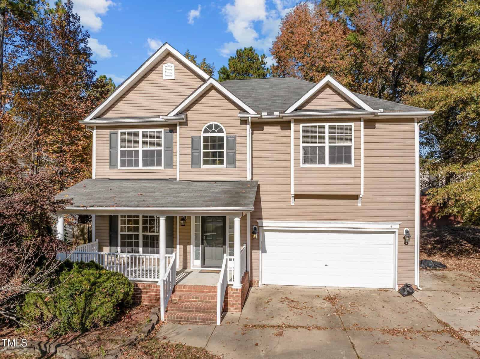 The two-story beige house on 1608 Irving Place boasts gray shutters and white trim, with a charming covered front porch and double garage. Nestled in the autumn trees of Creedmoor, its driveway and front steps welcome you to a clear sky dotted with a few clouds.