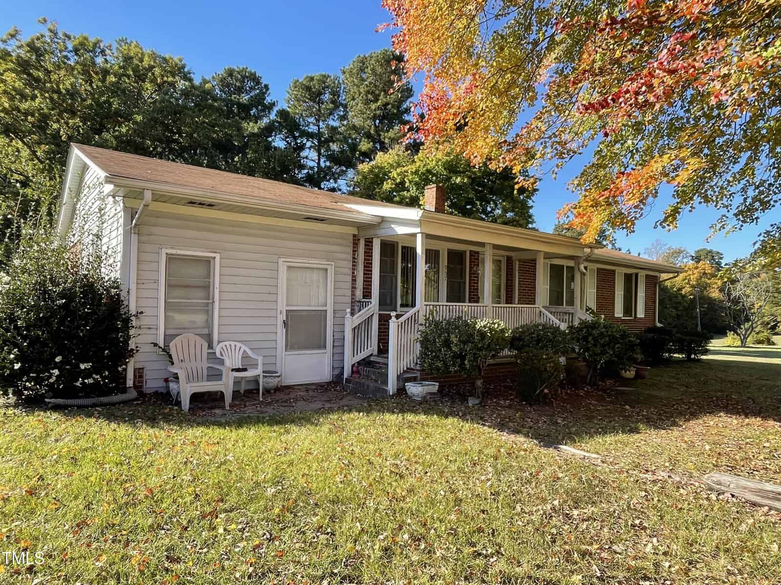 Nestled on 957 County Line Road in Manson, this charming single-story house features white siding and a welcoming front porch. Surrounded by green grass and trees with vibrant autumn foliage, two white chairs sit invitingly by the side of the porch under a clear blue sky.