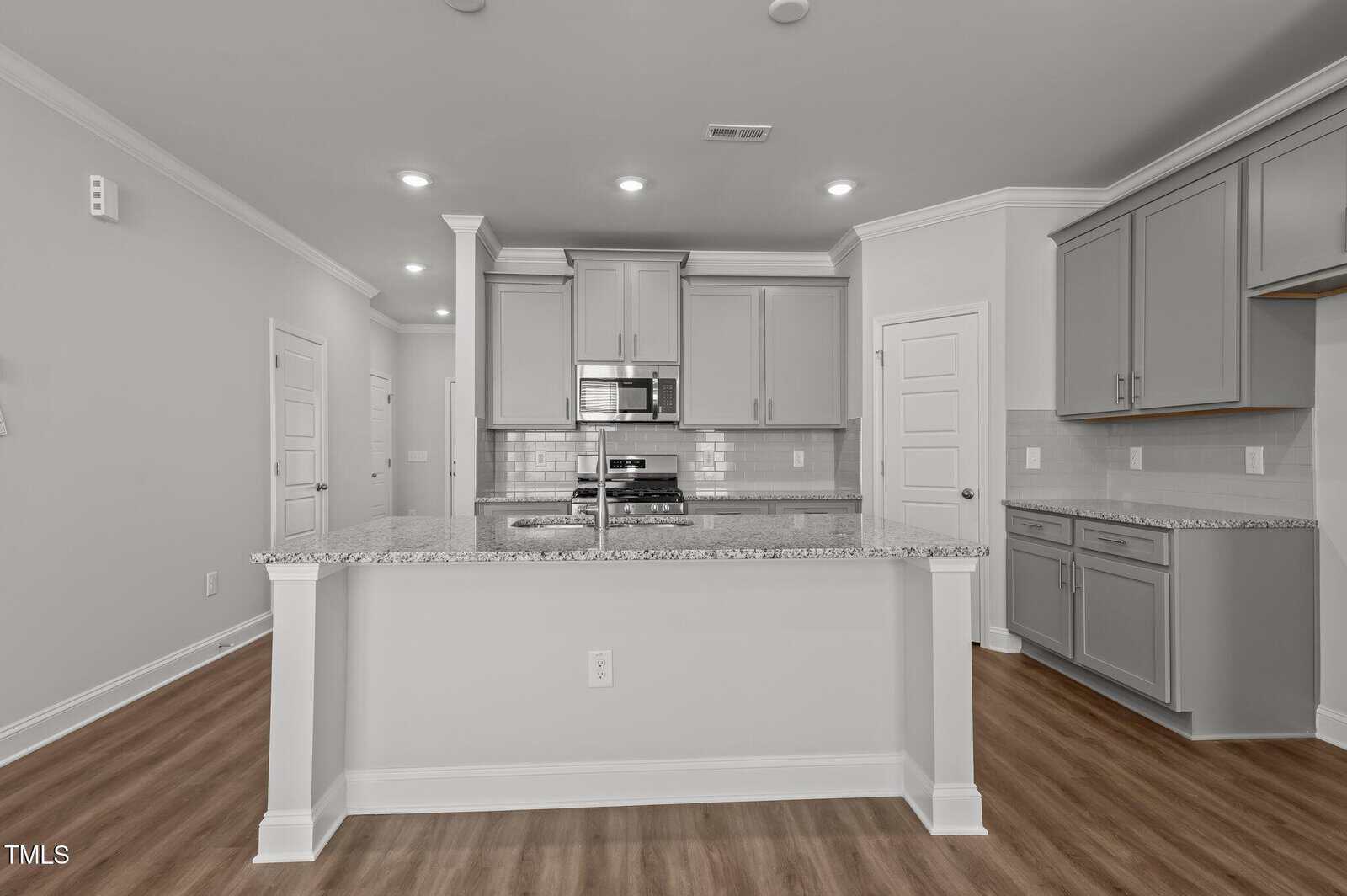 Modern kitchen with light gray cabinets, stainless steel appliances, granite countertops, white subway tile backsplash, and wood-look flooring. The kitchen is well-lit with recessed ceiling lights.