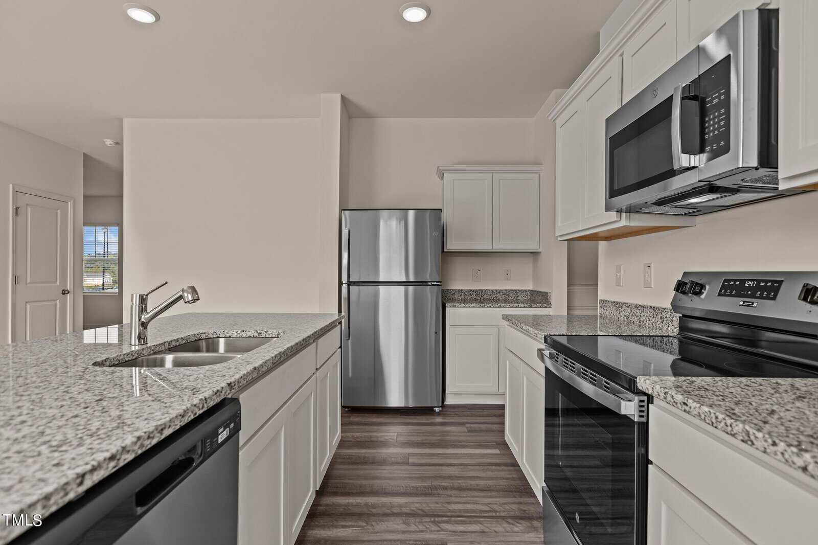 Modern kitchen with white cabinets, stainless steel appliances including a refrigerator, oven, microwave, and dishwasher, granite countertops, and wood-style flooring. Bright and clean with a neutral color palette.