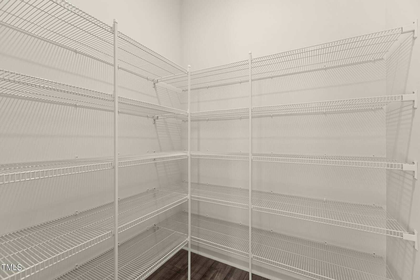 Empty walk-in pantry with white wire shelving on two walls and a dark wood floor, creating ample storage space in a clean, well-lit room.