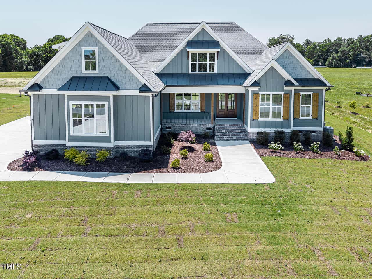 A modern gray and white single-story house at 70 Water Willow Lane, Zebulon, featuring a front porch, gabled roof, large windows, landscaped garden beds, and a driveway, surrounded by a green lawn and open grassy area.