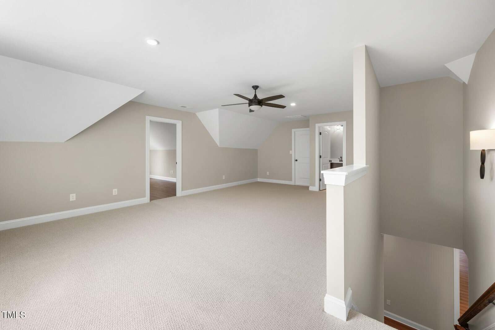 A spacious, carpeted upstairs room with beige walls, a ceiling fan, recessed lighting, and multiple doorways leading to adjacent rooms. A stairway with a white railing appears in the right foreground.
