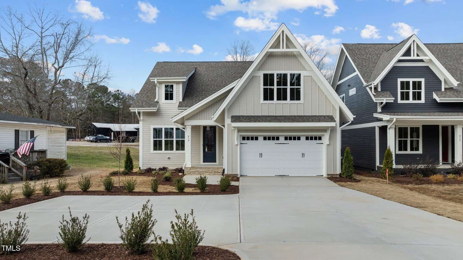 A modern two-story house with light siding, a steep roof, and a double garage sits between two other homes on 418 S Cross Street in Youngsville. The concrete driveway leads to the home, with small shrubs planted along the front yard and trees visible in the background.