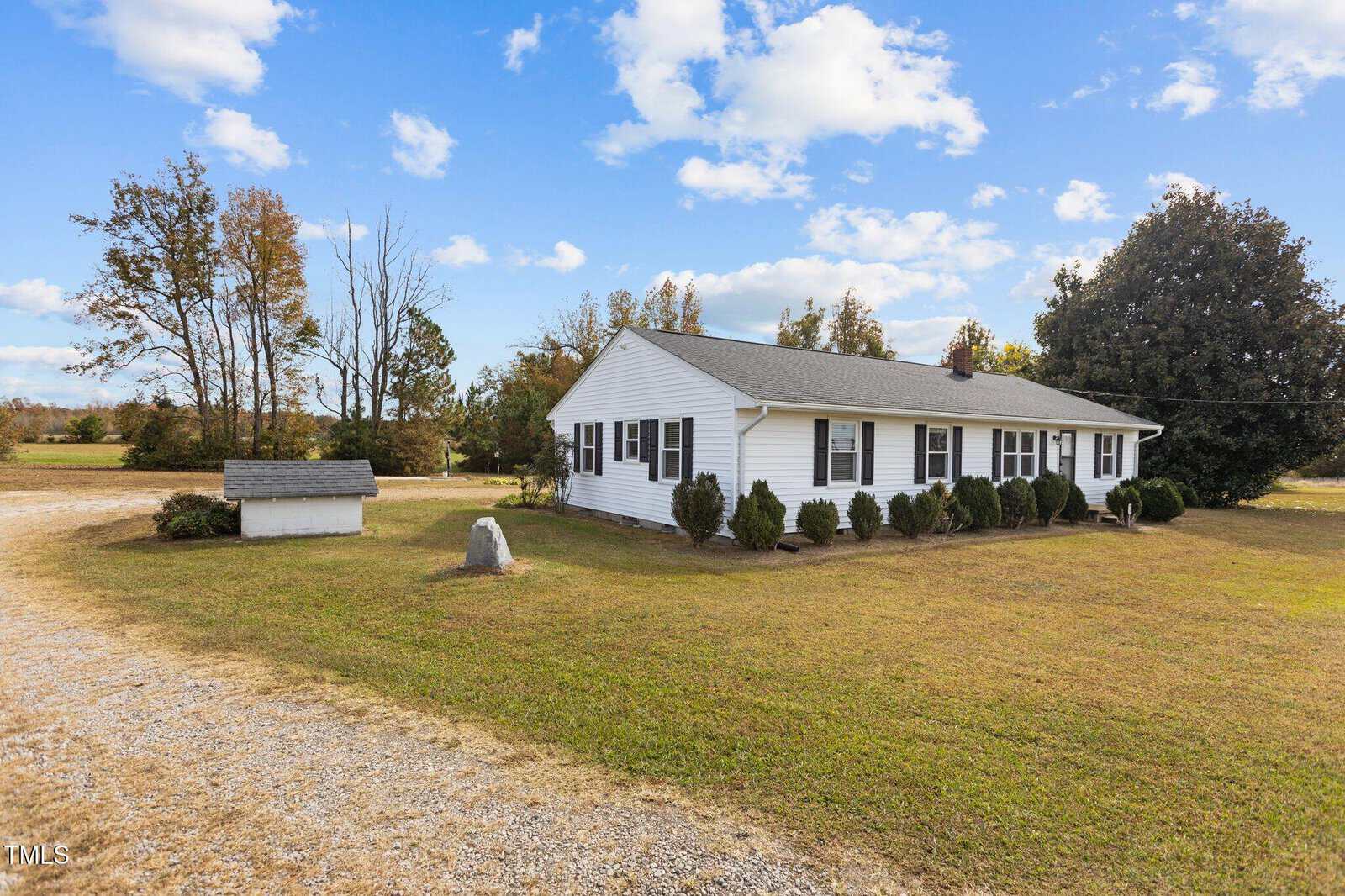 Located at 6206 Huntsboro Road, Oxford, this charming white single-story house features a gray roof and green shutters. It's nestled on a grassy lawn with shrubs lining the front. A gravel driveway guides you home, while a small shed rests peacefully under the clear blue sky with scattered clouds.