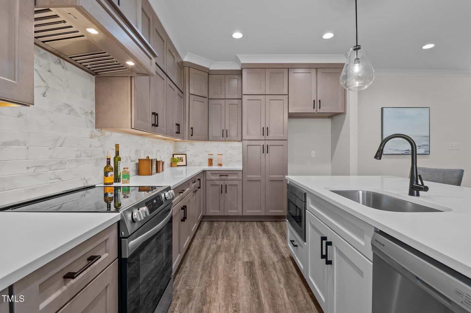 Modern kitchen with light wood cabinets, white countertops, stainless steel appliances, and a marble backsplash. Pendant lighting hangs above the island with a sink and faucet. The floor is wood-style laminate.