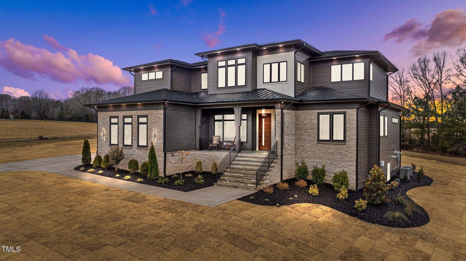 A modern two-story house at 30 Hartwood Lane in Youngsville features large windows, gray siding, and stone accents. The front steps lead to a covered entrance, with minimal landscaping on a spacious lot captured at dusk.