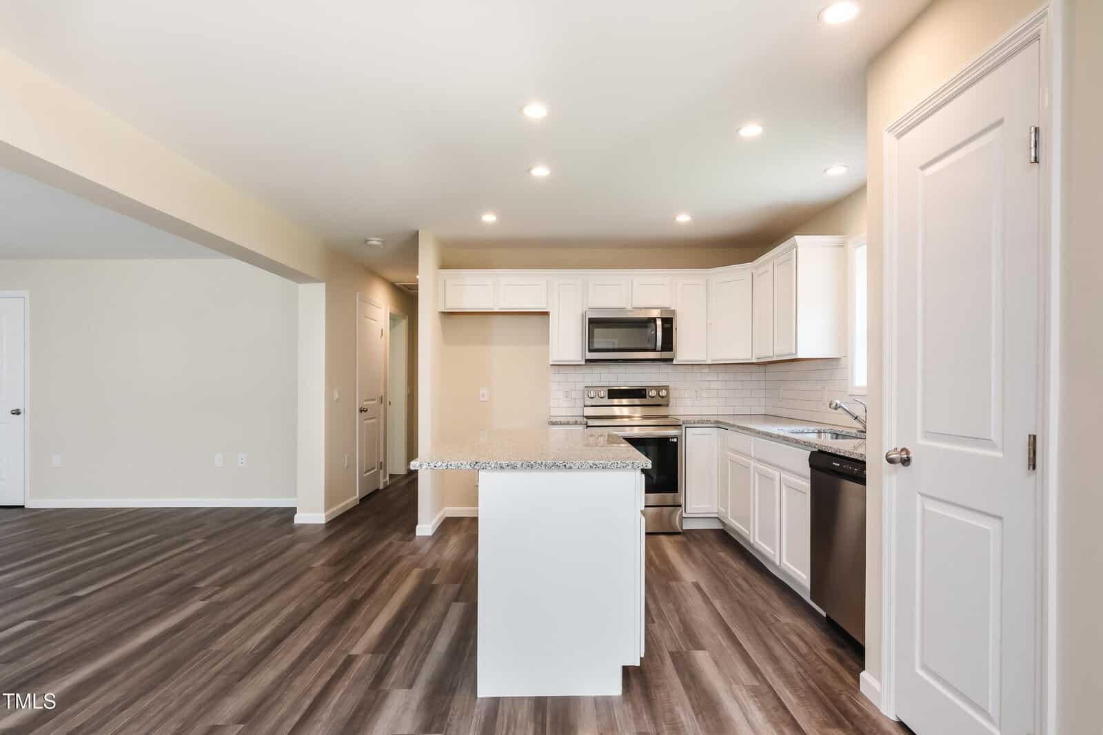 Modern kitchen with white cabinets, stainless steel appliances, a center island with granite countertop, subway tile backsplash, and wood-look flooring. Room is brightly lit with recessed lighting.