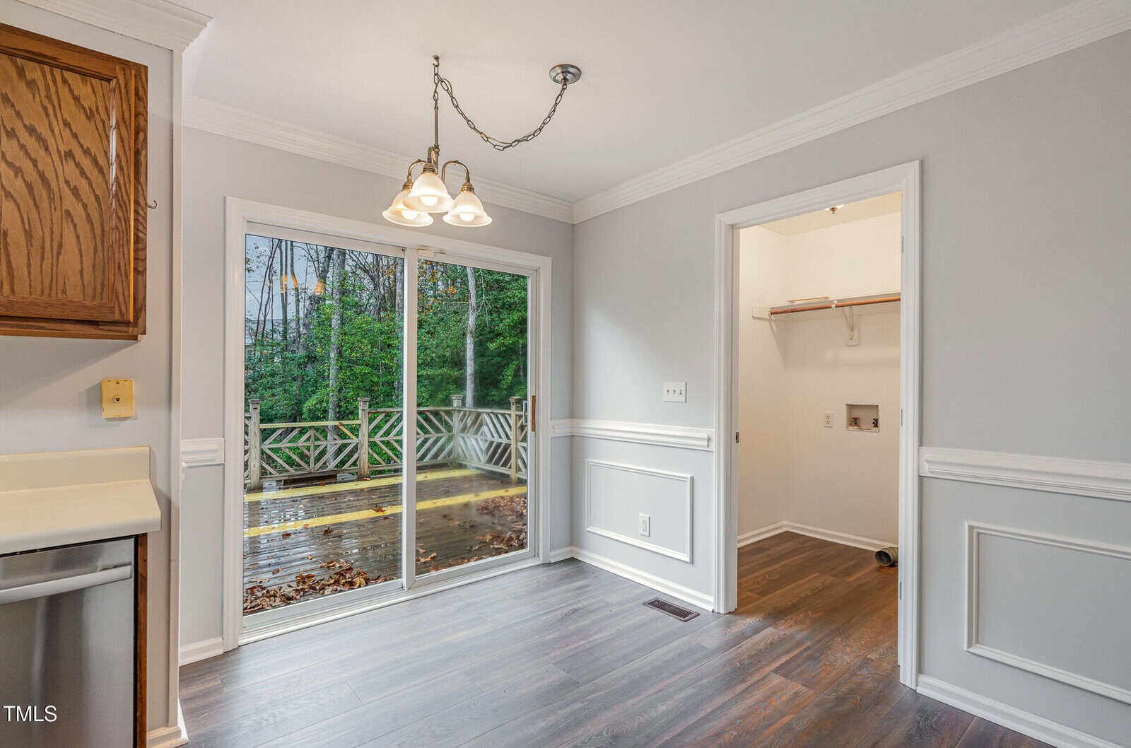 A dining area with a sliding glass door leading to a deck outside. The room has gray walls with white trim, wood floors, a ceiling light fixture, and an adjacent laundry nook with shelves.
