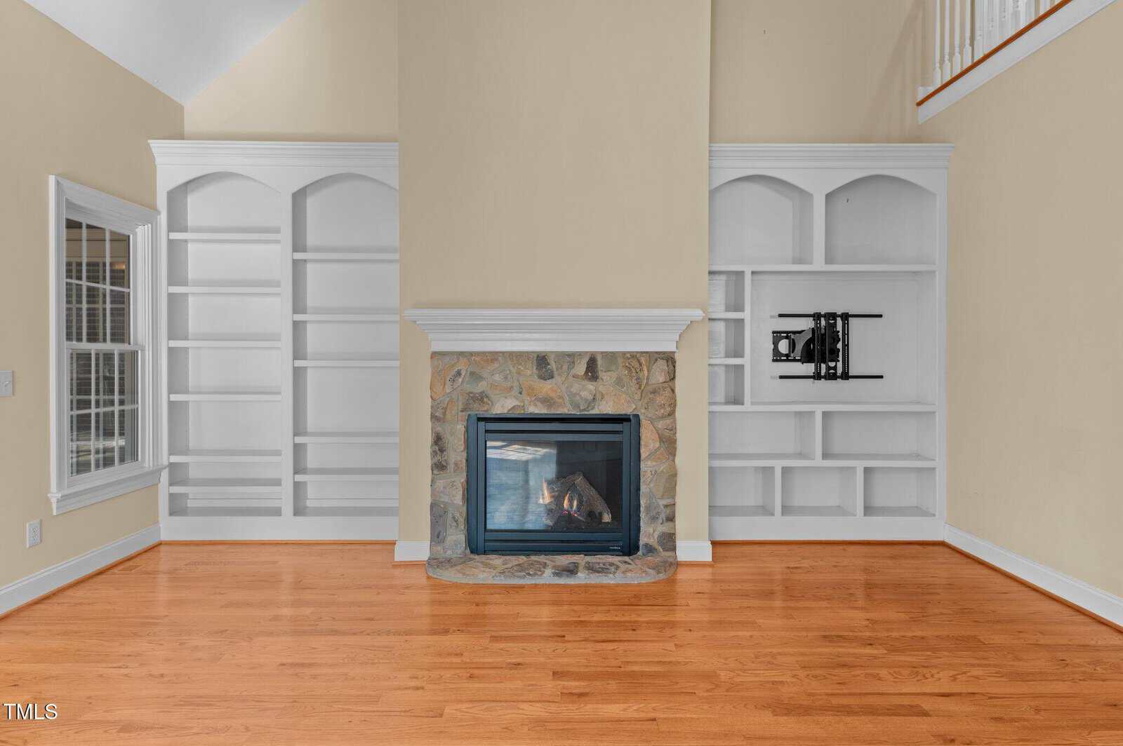 Living room with hardwood floors, a stone fireplace in the center, and built-in white shelves on both sides. The shelves on the right hold a few items, while those on the left are empty.