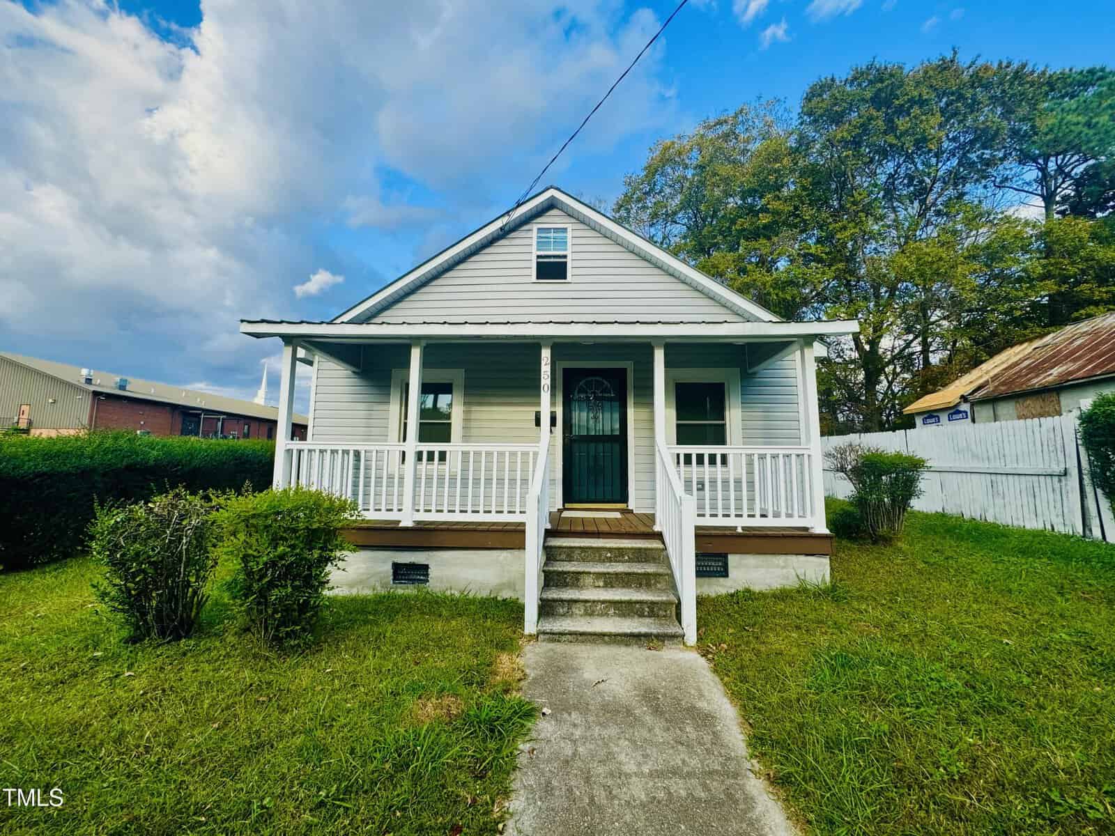 Located at 250 Horner Street in Henderson, this charming small, single-story house features light gray siding and a welcoming front porch. Adorned with white railings, the porch overlooks a grassy lawn under a partly cloudy sky with trees in the background.