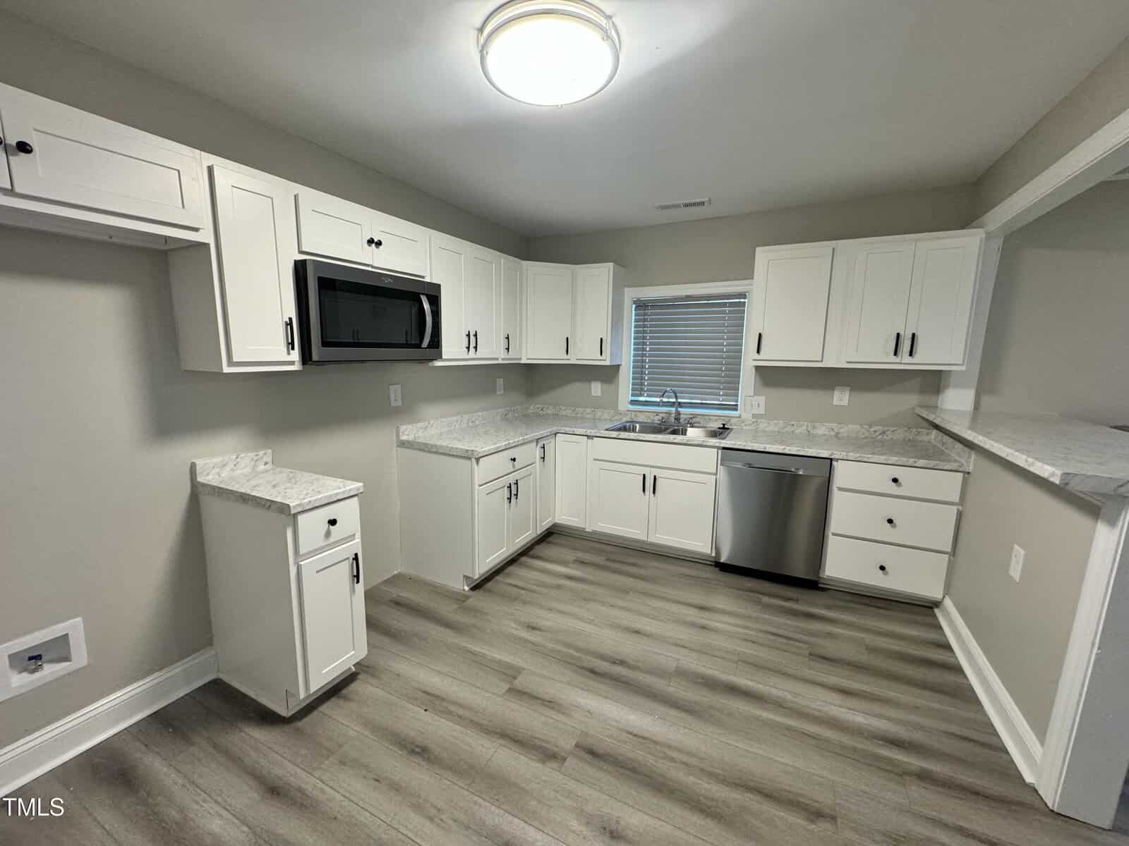 Modern kitchen with white cabinets, granite countertops, stainless steel appliances, and light wood flooring. Features a large window above the sink, providing natural light.