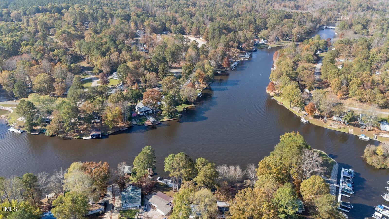 Aerial view of a wooded lakeside residential area with houses scattered among trees, docks along the shore, and a winding body of water running through the center of the image.