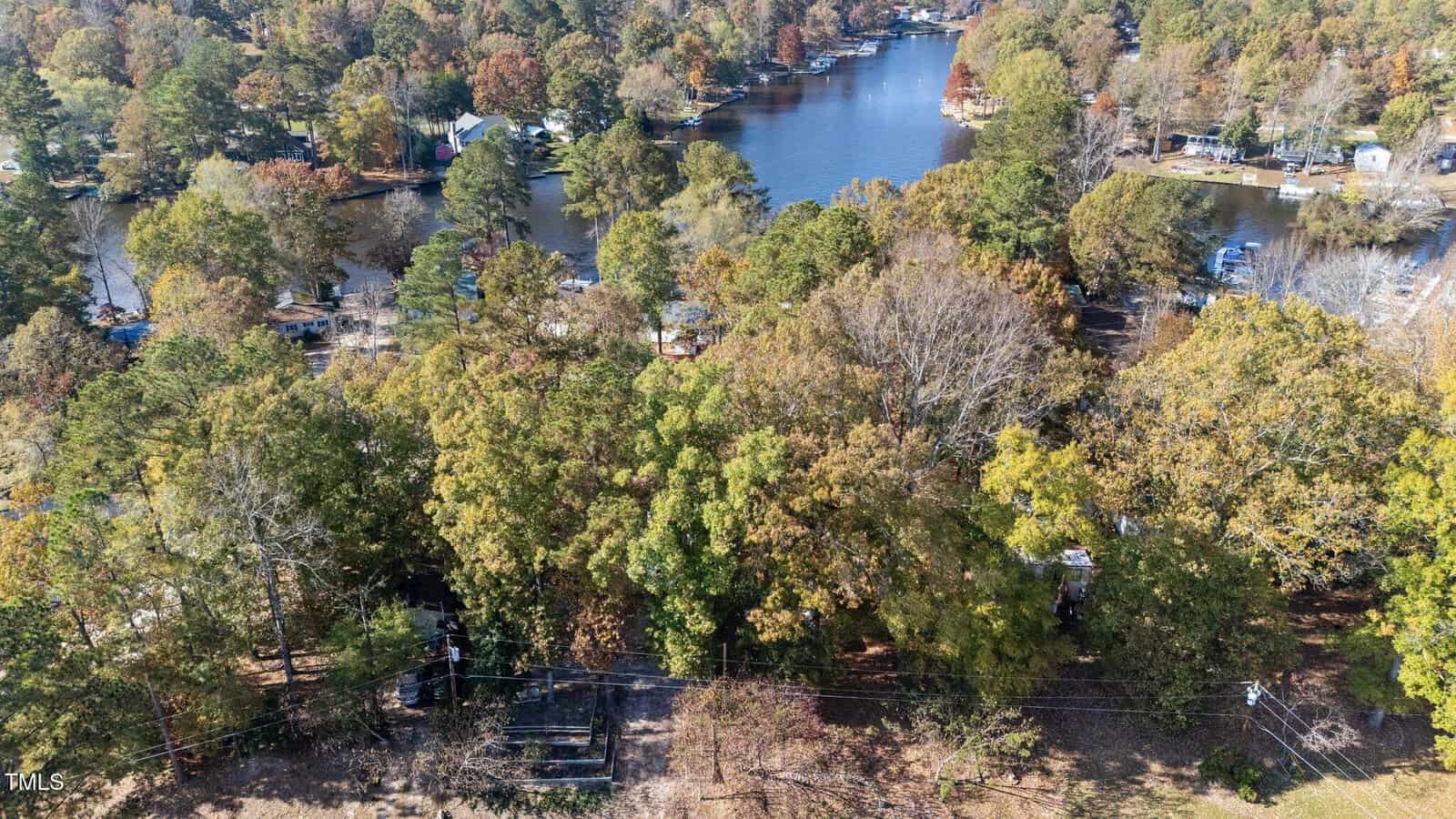 Aerial view of a wooded area with houses scattered among trees, a river or lake in the background, and power lines running along the bottom of the image.