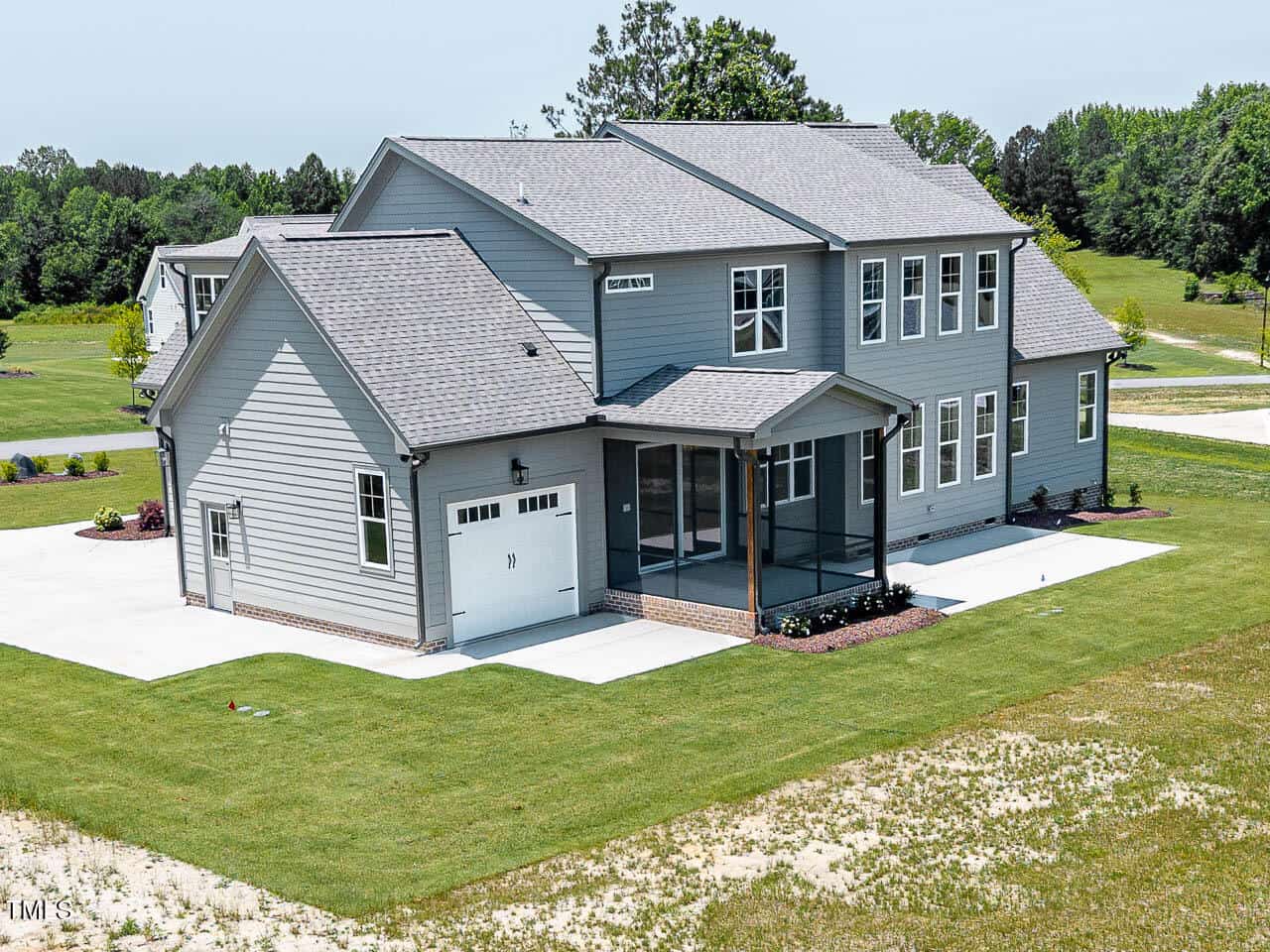 A modern two-story gray house with a screened porch, attached garage, and large concrete driveway, surrounded by a well-kept lawn and trees in the background.
