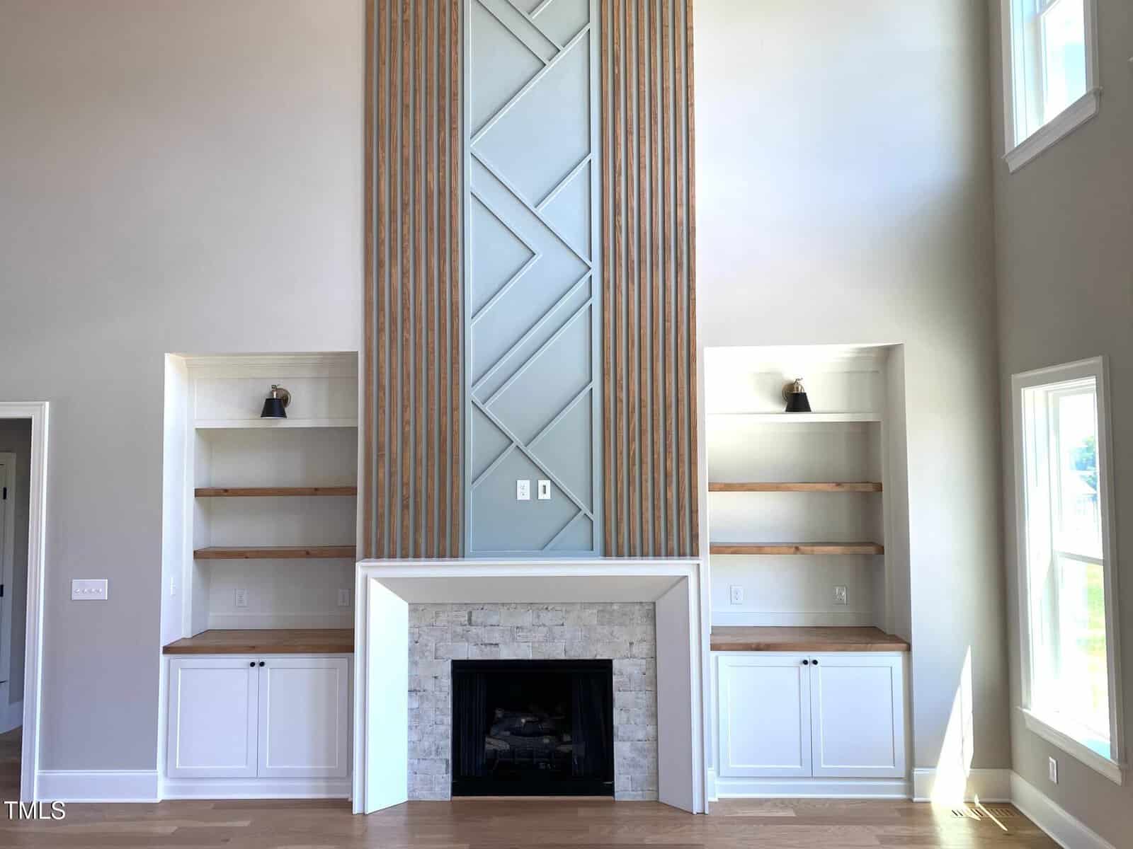 Modern living room with a tall fireplace, geometric blue paneling, light stone surround, flanked by built-in shelves and cabinets. High ceiling and large windows let in natural light.
