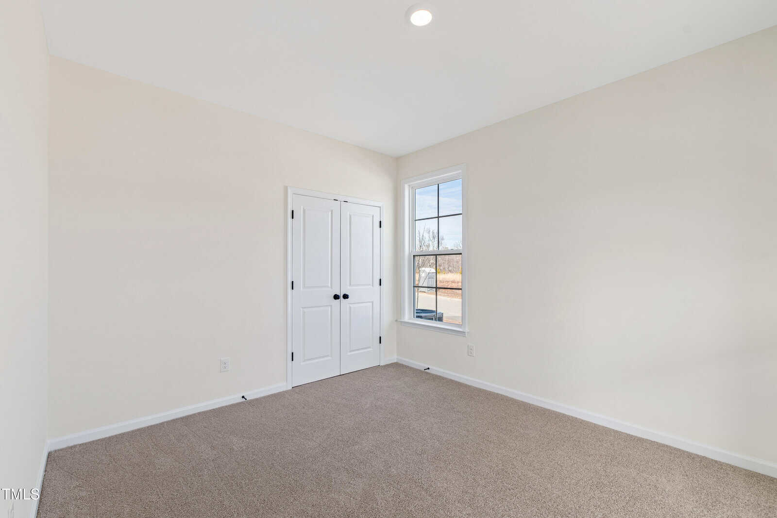 Bright, empty room with beige walls, carpeted floor, double-door closet, and a large window letting in natural light.