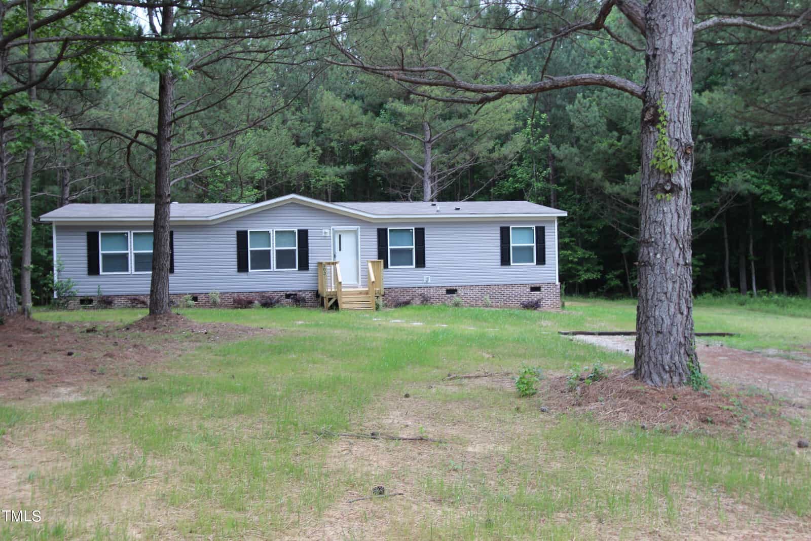 Located at 583 Madison's Grove Lane, this single-story gray house with white trim sits in a clearing surrounded by trees in Henderson. The home features a small wooden porch and steps leading to the front door, while the yard is a blend of dirt and sparse grass.