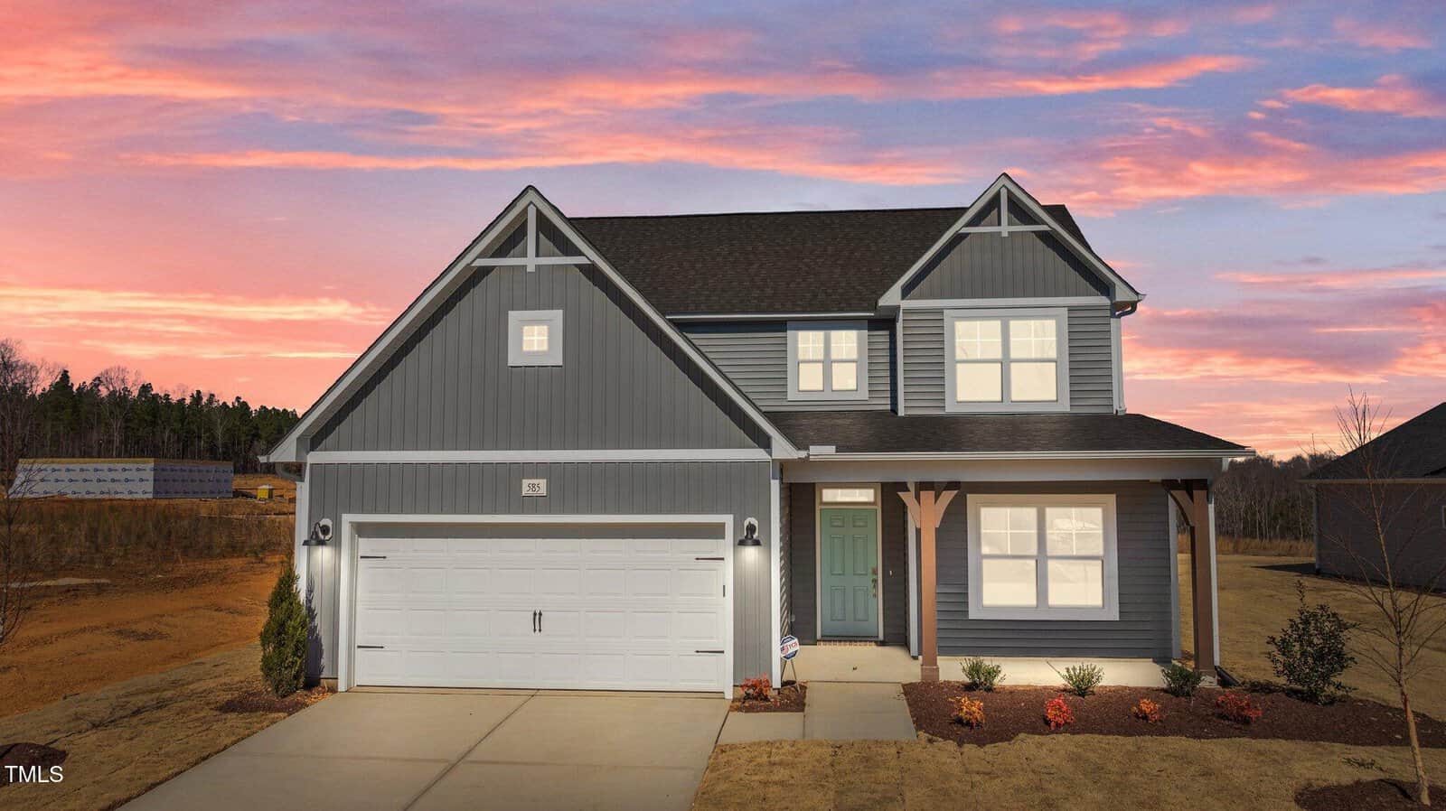 A two-story gray house with white trim and a double garage, viewed at sunset. The front yard has minimal landscaping, and the house features a covered porch with wooden posts.
