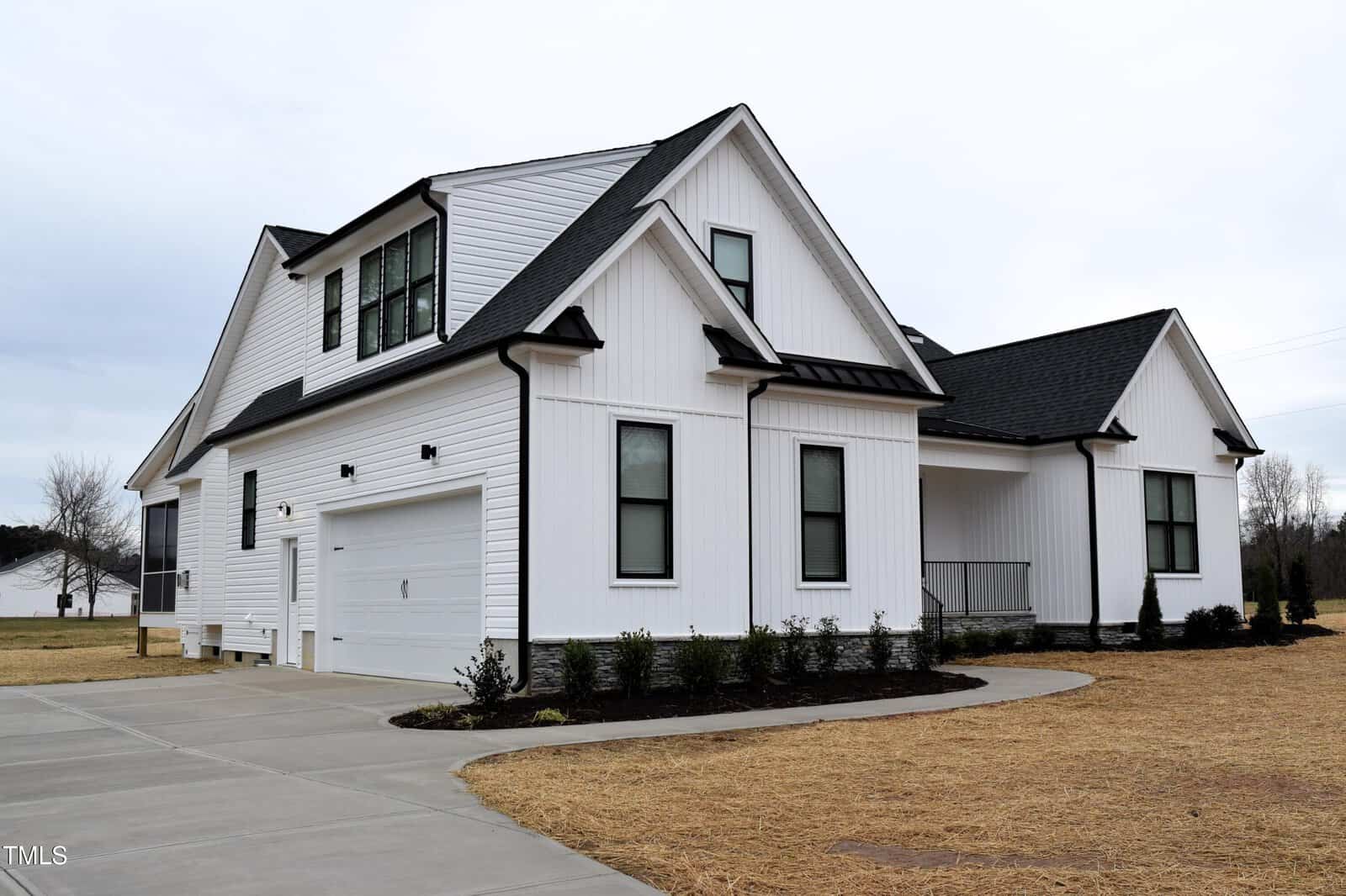 Located at 4300 Bragg Farm Lane in Franklinton, this modern white house boasts a sleek black roof and numerous windows. It features a two-car garage and a curved driveway. The yard, tinged brown from dry grass, mirrors the overcast sky above.