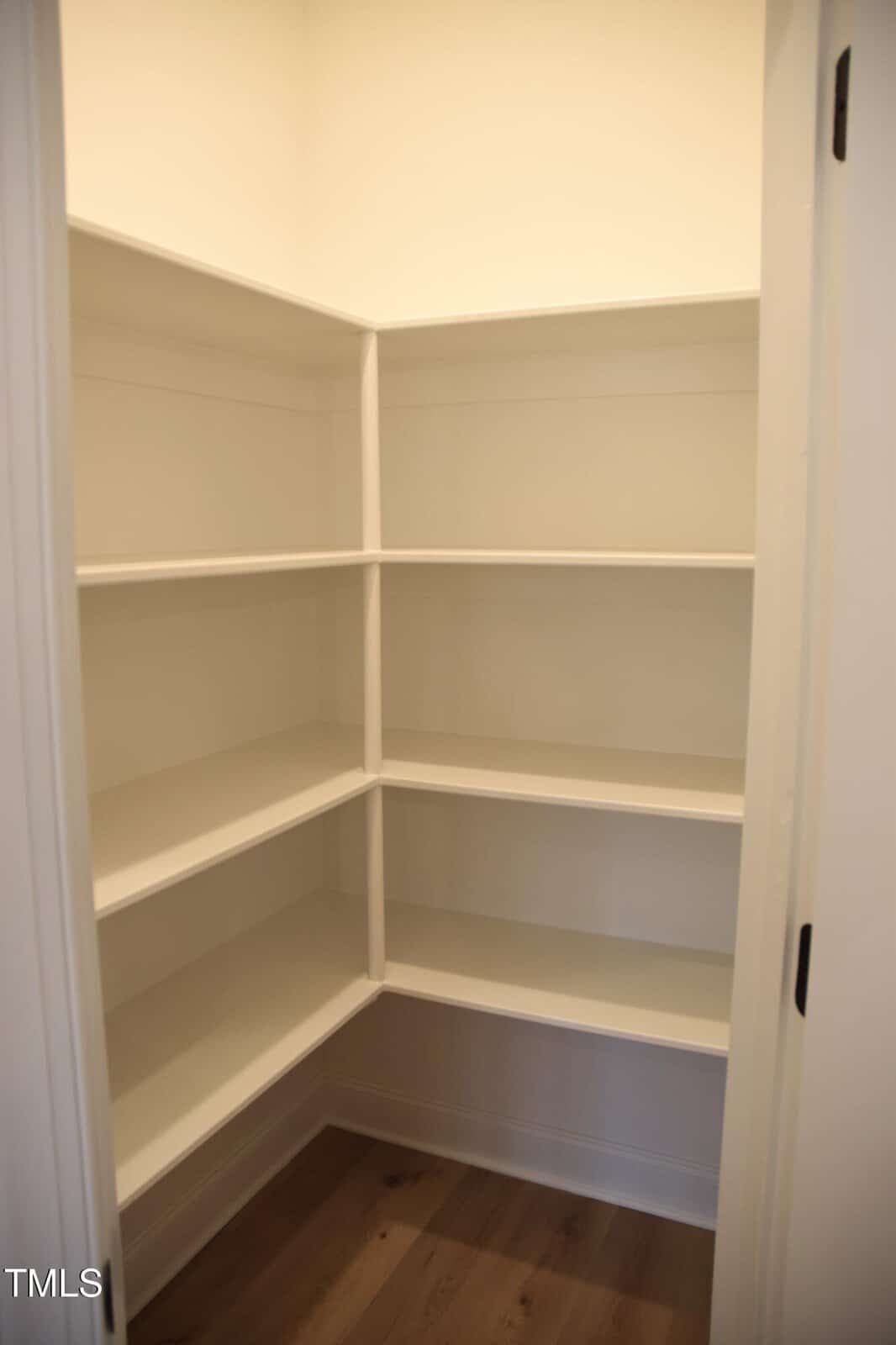 A small empty pantry with white built-in shelves on three walls and a wooden floor. The shelves are evenly spaced, creating ample storage space. The room is well-lit, with a simple and clean design.