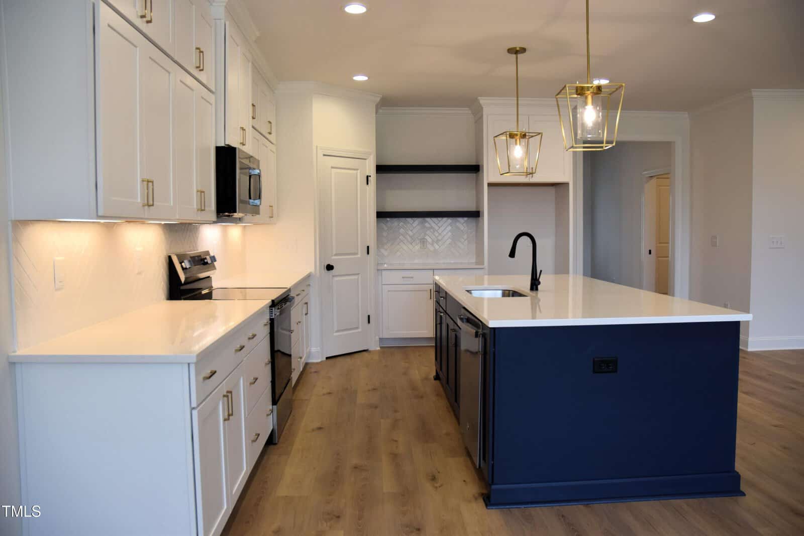 A modern kitchen featuring white cabinets, a large blue island with a white countertop, and two hanging pendant lights. The room has wood flooring and stainless steel appliances, including a stove and a built-in microwave.