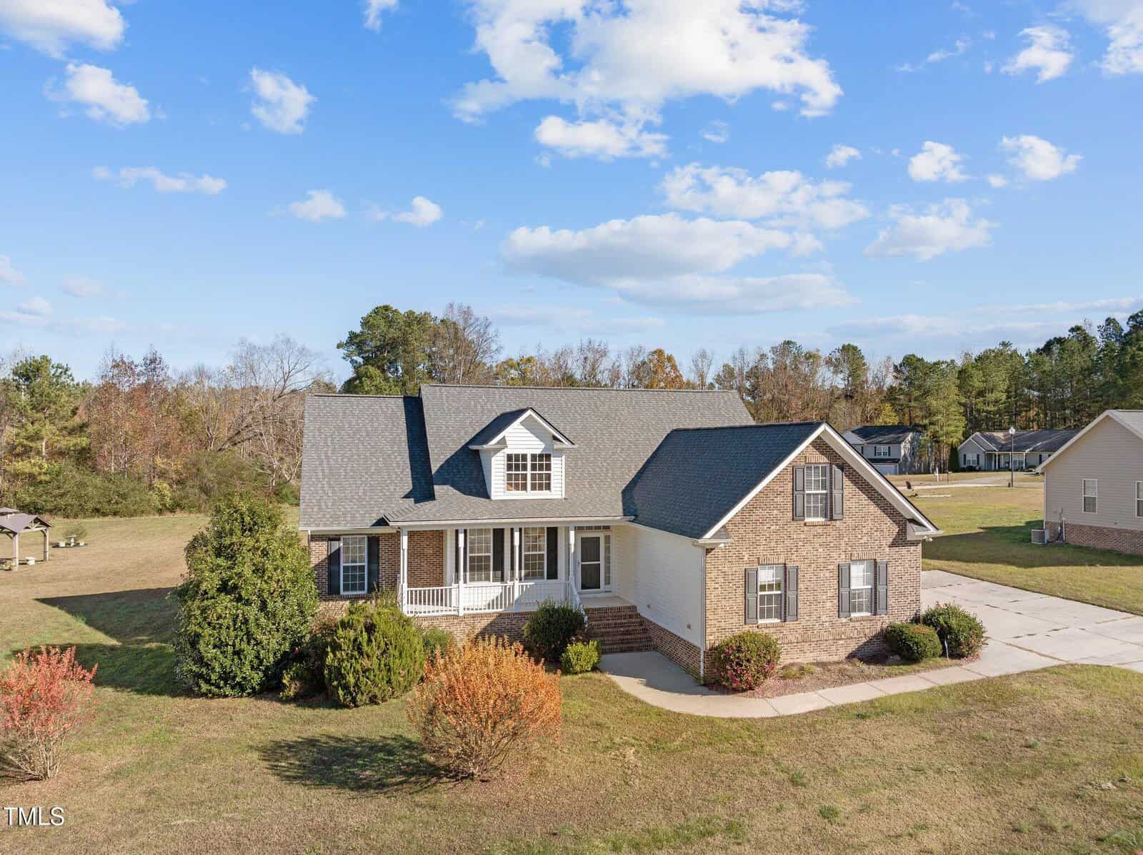 A single-story brick house on 206 W Waycliff Road in Henderson, featuring a gray roof, a front porch, and two dormer windows. It's nestled on a grassy lot with shrubs and trees under a clear blue sky with scattered clouds. A neighboring house is partially visible.