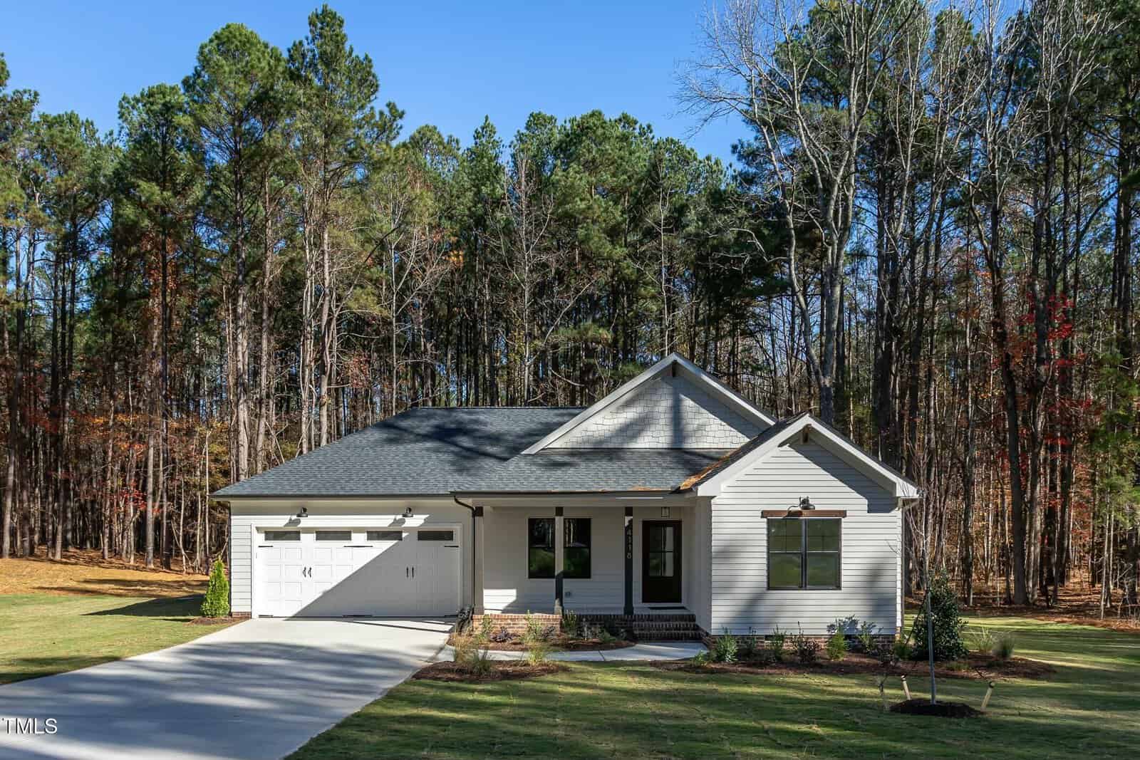 Nestled at 4118 Emily Lane, Oxford, this single-story house boasts a light gray exterior and dark roof, surrounded by a wooded area. It features a two-car garage, small front porch, and a neatly maintained lawn connected by a welcoming driveway.