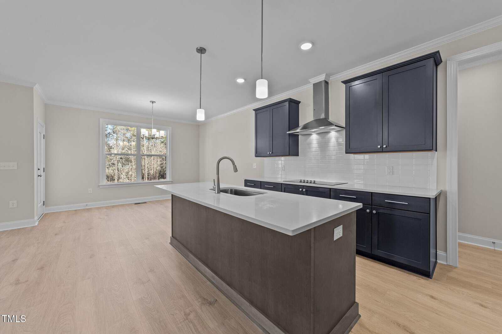 Modern kitchen with navy cabinets, white countertops, stainless steel appliances, island with sink, light wood floors, hanging pendant lights, and a large window letting in natural light.