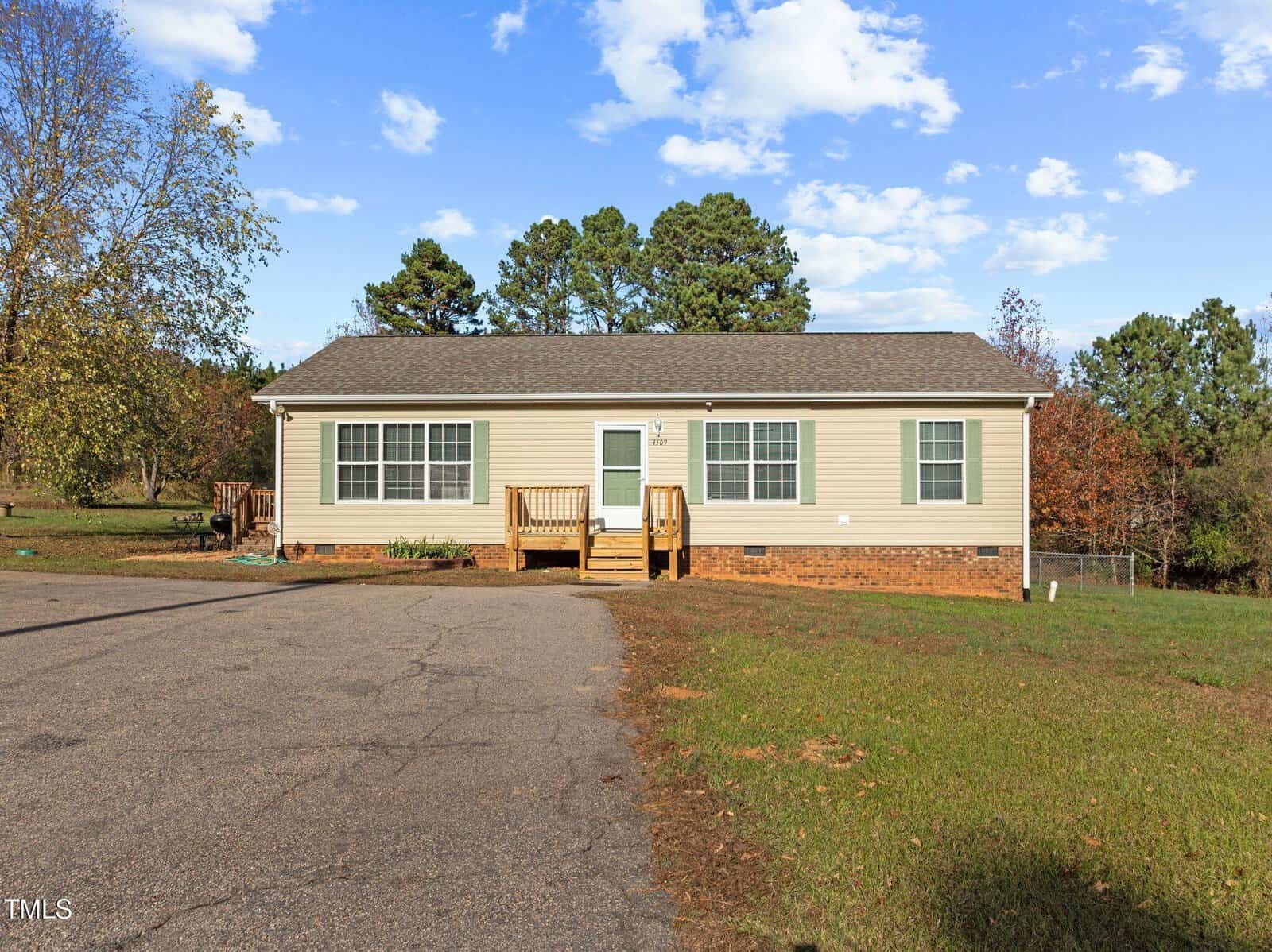 A single-story house with beige siding and a brown shingled roof, located at 4509 NC Hwy 56 in Franklinton. It features a small front porch with steps leading to the entrance, set on a large paved area surrounded by grass and trees under a partly cloudy sky.