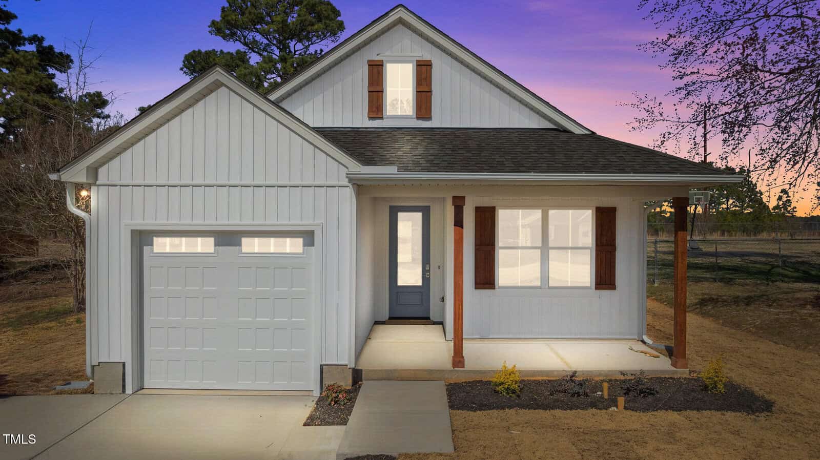 A single-story white house with a gable roof, attached one-car garage, front porch with wooden posts, brown shutters, and a concrete driveway, photographed at dusk with a purple and orange sky in the background.