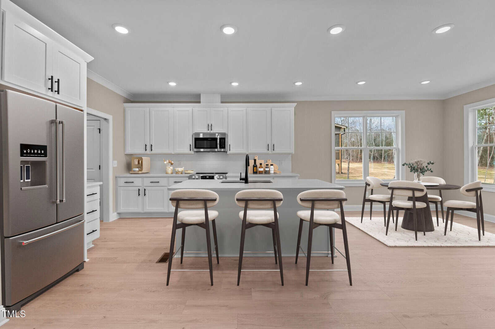 Modern kitchen with white cabinets, stainless steel appliances, a center island with four bar stools, and an adjacent dining area with a table and six chairs next to large windows overlooking a yard.