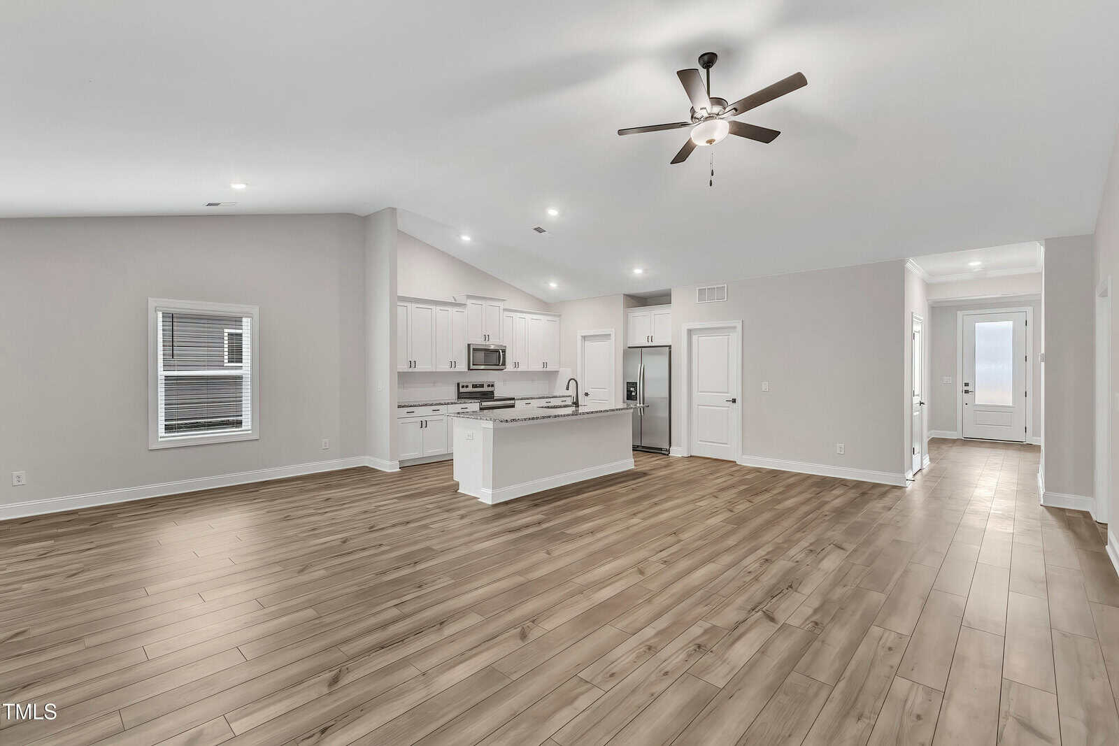 Open-concept living space with wood flooring, white walls, and recessed lighting. Features a modern kitchen with white cabinets, stainless steel appliances, and an island. Ceiling fan is installed above the main area.